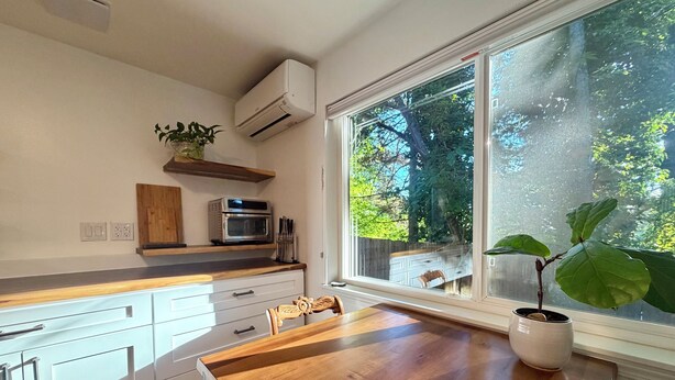 Eine Küche mit weißen Schränken, einer Holzausziehtafel, einem Backofen und einem Fenster mit Blick auf Bäume.