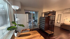 Ein modernes Interieur mit einem Holzesstisch, einer Zimmerpflanze, einem weißen Kühlschrank und einer Glastür zum Außenbereich.