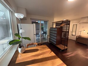 A modern interior with a wooden dining table, a potted plant, a white refrigerator, and a sliding glass door leading to an outdoor area. - Backyard Studio Near Lake WA, UW, & Hospitals (Seattle)