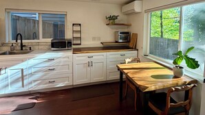 Eine Küche mit weißen Schränken, einer Holz Arbeitsplatte, einem Spülbecken, einer Mikrowelle, einem Backofen, einem Fenster mit Blick auf Bäume und einem Essbereich mit Tisch und Stühlen.
