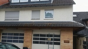 A two-story building with a garage, a sign indicating a business, and a flower pot. - Holiday Apartment An Der Lempe with Wi-Fi (Hofgeismar)