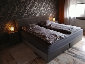 Une chambre moderne avec un mur en marbre, un lit avec une literie grise et deux lampes de chevet.