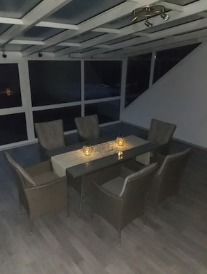 Ein moderner Essbereich mit einem rechteckigen Tisch, sechs Stühlen und Blick auf den Nachthimmel durch große Fenster.