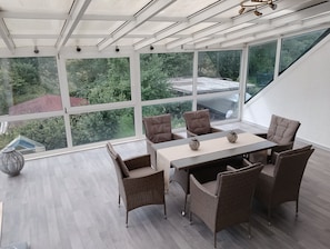 Un espace repas comprenant une table et des chaises, de grandes fenêtres et une vue sur la verdure.