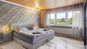 A bedroom with a bed, nightstands, a window with curtains, and a view of the outdoors. - Holiday Apartment An Der Lempe with Wi-Fi (Hofgeismar)