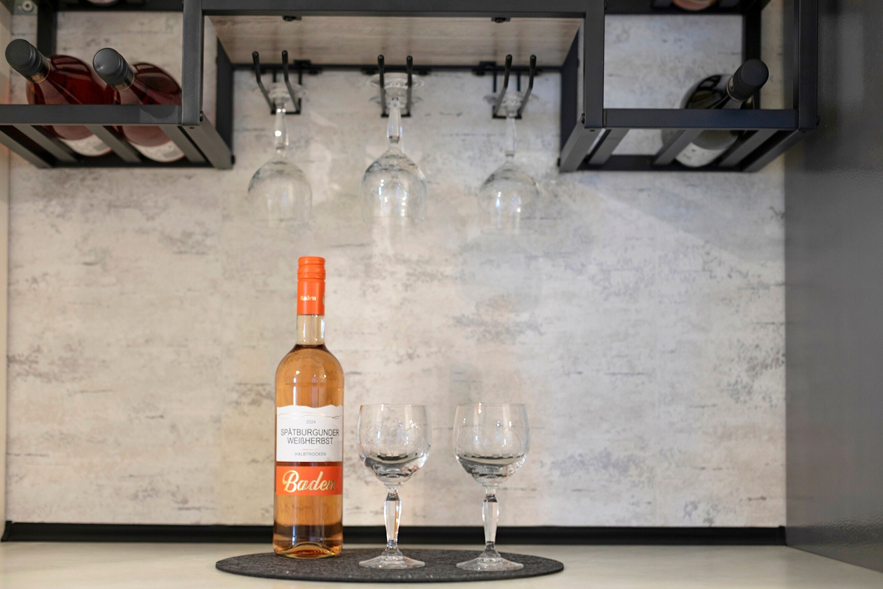 A bottle of wine and two glasses on a coaster, with a wine rack in the background.