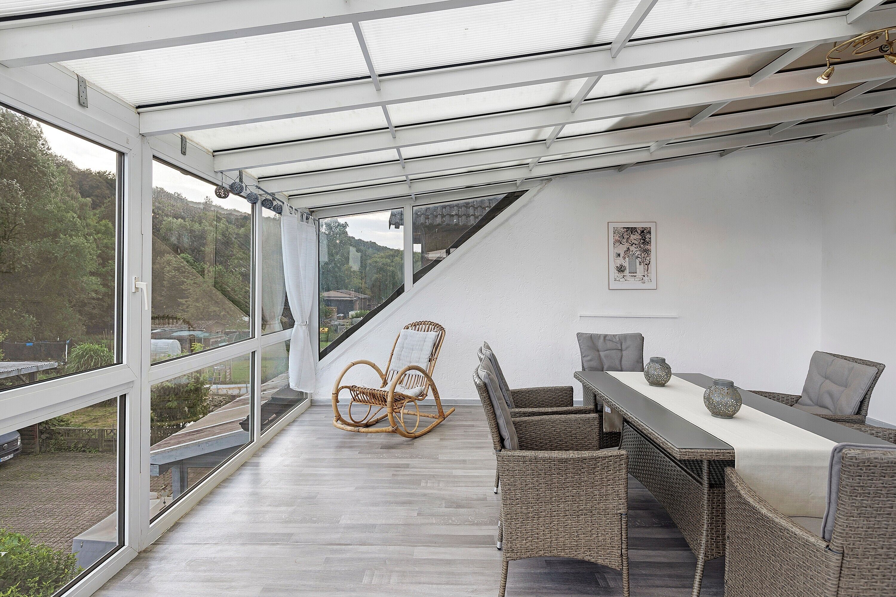A conservatory with a dining area, wicker furniture, and a view of the outdoors.