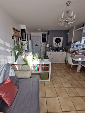 A modern living room with a sofa, a dining area with a table and chairs, a kitchen area, and a chandelier. - Spacious and cozy apartment with a flower-filled terrace in downtown Annecy (Annecy)
