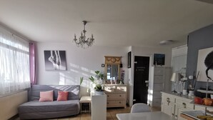Un saló modern amb un sofà gris, una taula de dinar i una cuina amb armaris i un taulell.