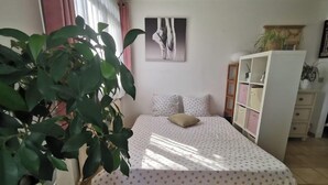 Un dormitori amb llit, una tauleta de nit, un prestatge i una planta en test.