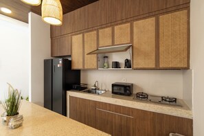 A kitchen with wooden cabinets, a black refrigerator, a microwave, and a gas stove. - Uluwatu 2 Bedrooms villa with Rooftop (Kec. Kuta Sel)