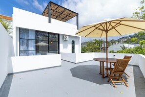 A modern outdoor patio with a table and chairs, a large umbrella, and a view of a cityscape. - Uluwatu 2 Bedrooms villa with Rooftop (Kec. Kuta Sel)