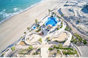 Vue aérienne d’un complexe hôtelier avec une piscine, des palmiers et une plage.