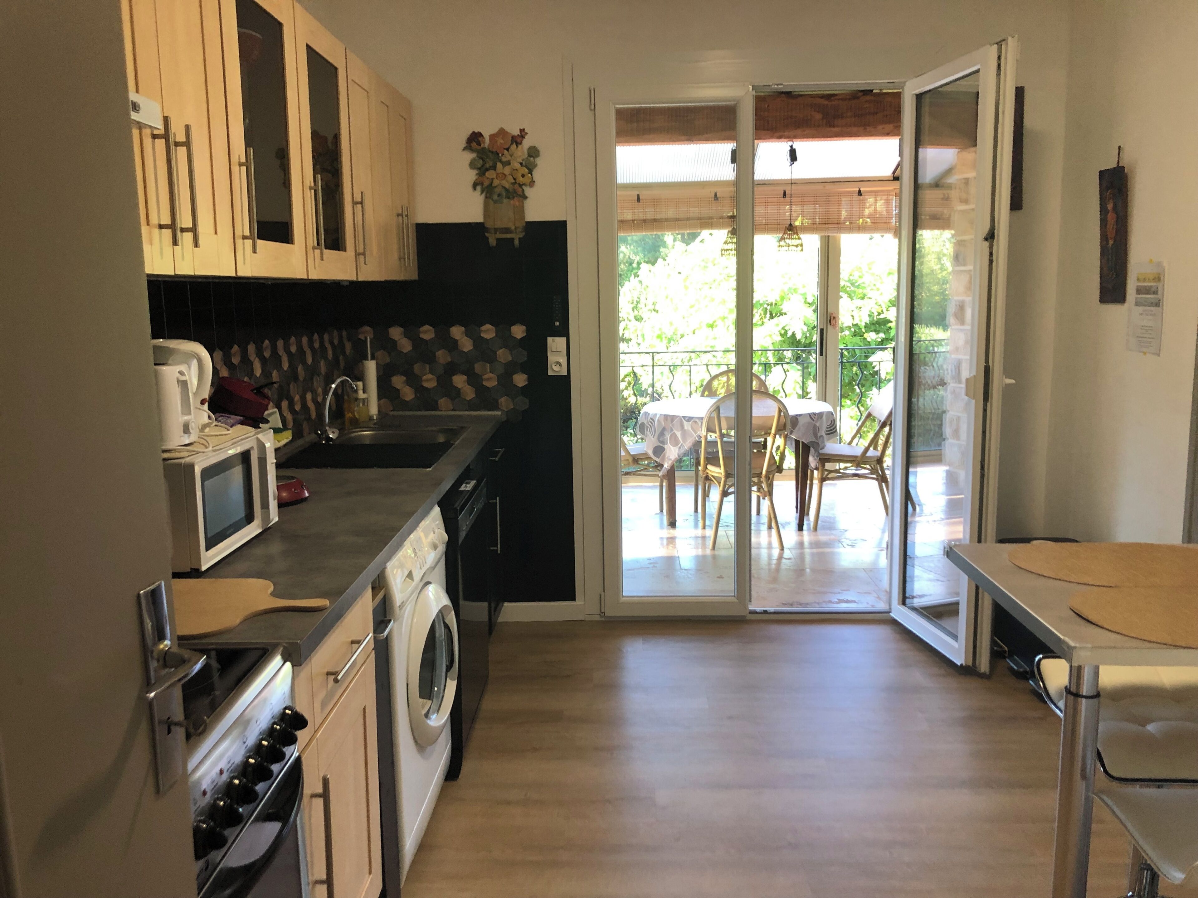 Une cuisine équipée d’un four à micro-ondes, d’une cuisinière et d’un lave-linge, un coin repas avec une table et des chaises, et une porte-fenêtre coulissante donnant sur une terrasse extérieure.