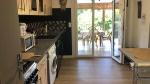 Eine Küche mit Mikrowelle, Herd und Waschmaschine, ein Essbereich mit Tisch und Stühlen sowie eine Glastür zu einer Terrasse.