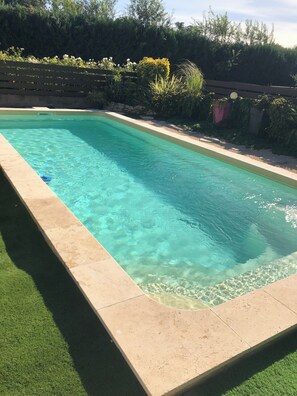 Une piscine rectangulaire à l’eau claire, bordée d’une margelle en béton et entourée d’une pelouse.