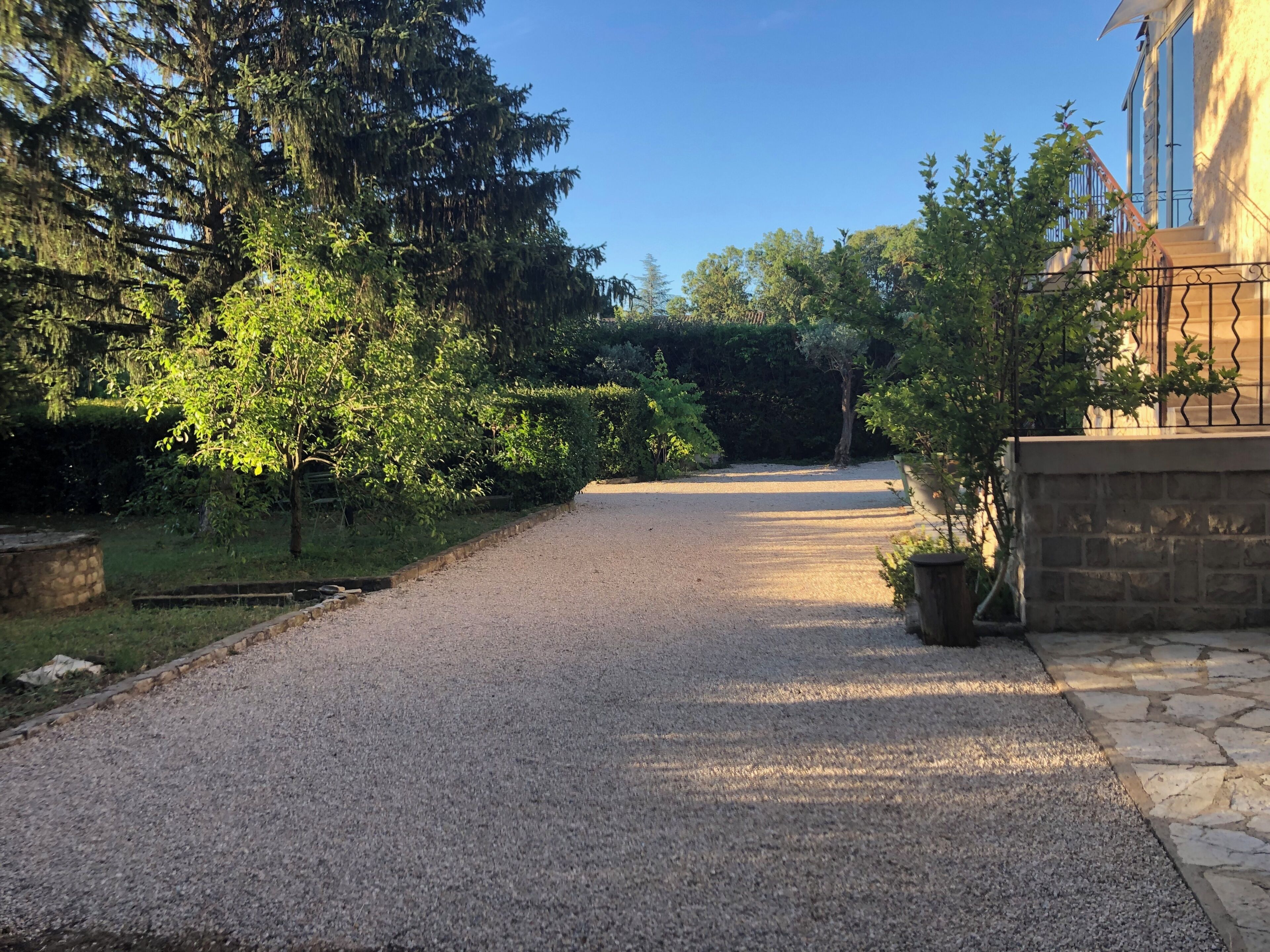 Une allée de gravier mène à une maison dotée d’un mur en pierre et d’une clôture en métal.