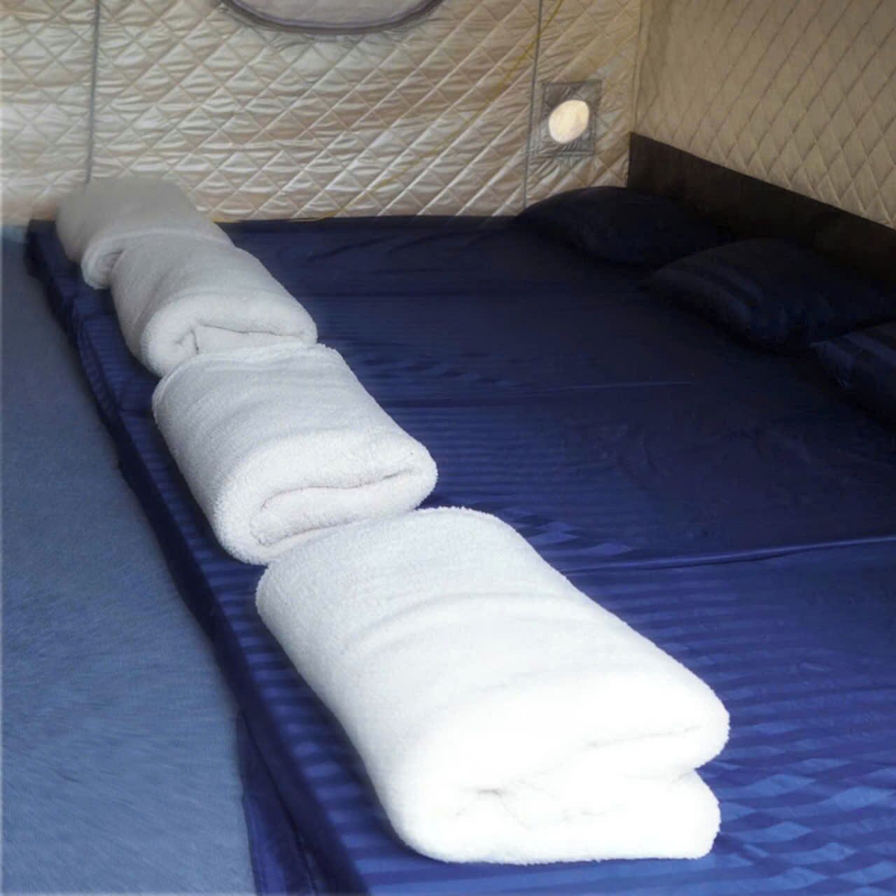 Cama bem arrumada com um edredom azul e uma toalha branca enrolada sobre ela.