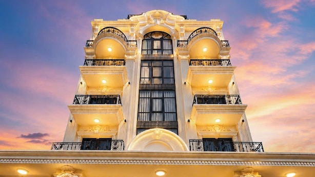 Una entrada imponente de hotel con un amplio arco, una gran escalera que sube y un candelabro colgante.