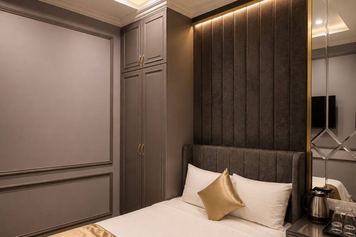 A hotel room with a large bed, a bedside table with a kettle, and a mirror.