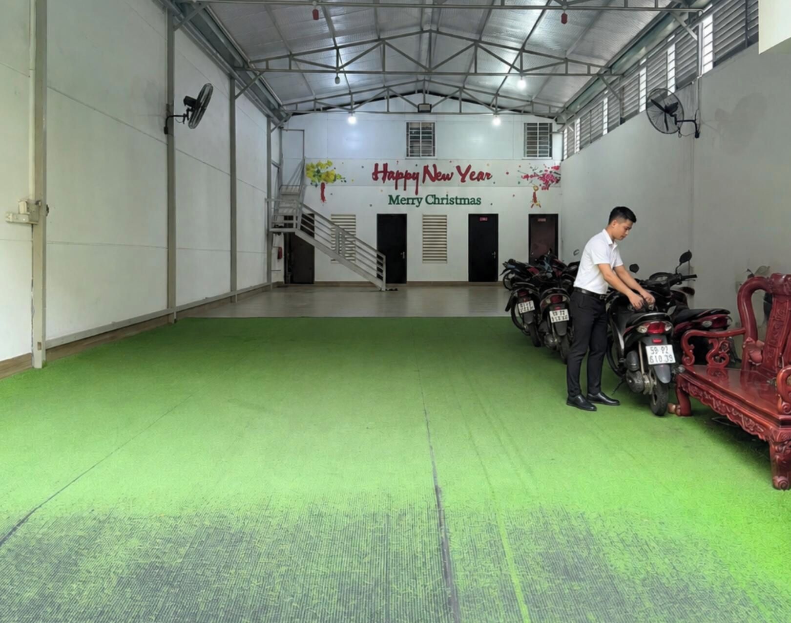 A spacious indoor area with a green floor, a staircase, and a row of motorcycles.