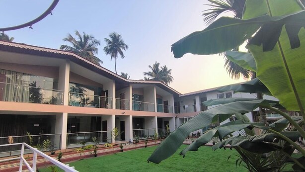 A multi-story building with balconies, a green lawn, and palm trees.