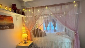 Une chambre à coucher avec un lit sous un dais, une table de chevet avec une lampe, un tapis moelleux et une étagère avec des objets décoratifs.
