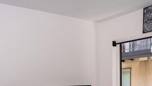 Un meuble de rangement blanc pour appareils électroniques, avec un téléviseur à écran plat, une plante en pot et une porte-fenêtre coulissante donnant sur un espace extérieur.