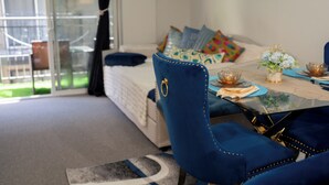 Un coin repas avec une table en verre, des chaises à l’assise bleue et un canapé agrémenté de coussins colorés.