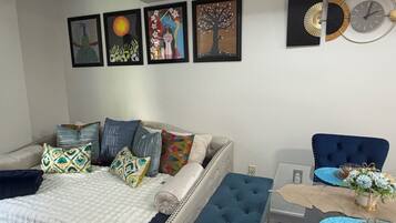 A bedroom with a bed, a blue armchair, a dining table with a vase, and wall art.