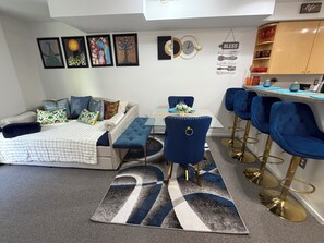 Ein modernes Wohnzimmer mit einer Couch, einem Esstisch und blauen Barhocker.