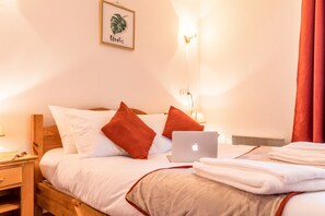 Ein ordentlich bezogenes Bett mit einem Laptop, Kissen und einem gerahmten Bild an der Wand.