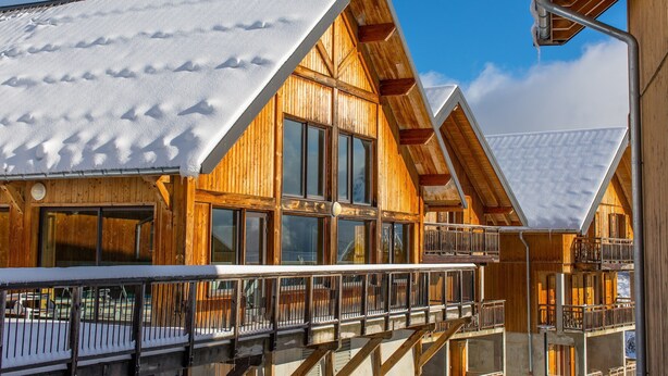 Una cabaña de madera con ventanas grandes y un balcón, rodeada de nieve.