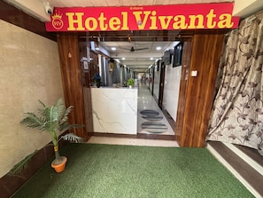 Ein Hotel mit Eingangsbereich, einer Rezeption, Kunstgräsern und einem Blumentopf.