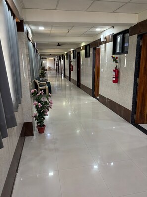 A hotel corridor with a shiny tiled floor, potted plants, and fire extinguishers on the walls. - HOTEL VIVANTA (ahmedabad)