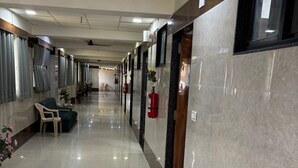 A hotel corridor with a shiny tiled floor, a sofa, potted plants, and fire extinguishers. - HOTEL VIVANTA (Ahmedabad)
