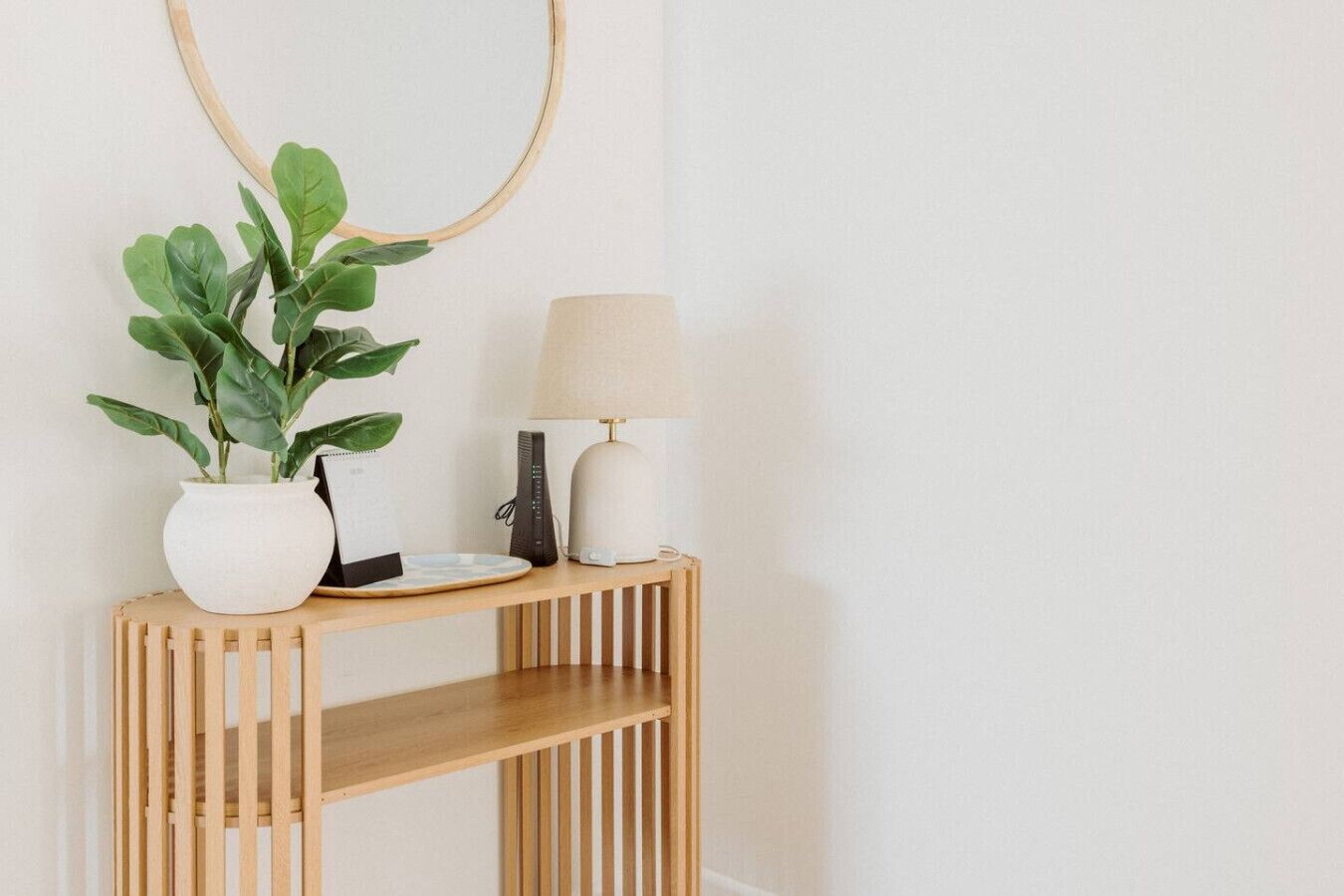 A wooden console table with a potted plant, a lamp, and a plate.