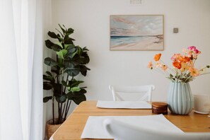 Ein Esstisch mit weißer Tischdecke, eine Blumenvase, ein Stuhl, eine Pflanze und ein Gemälde an der Wand.