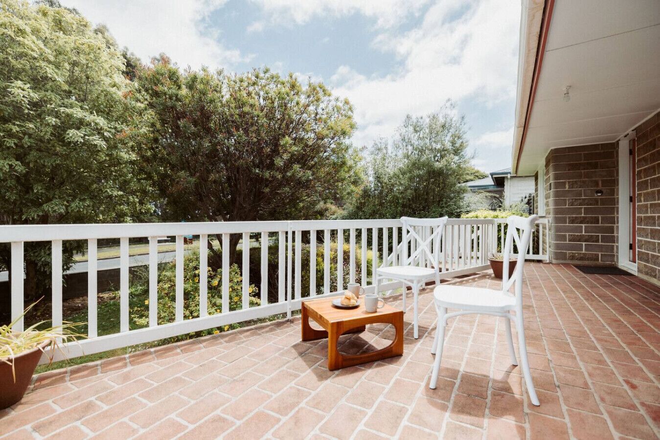 A balcony with a white railing, a wooden table, two white chairs, and potted plants.