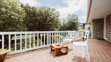 A balcony with a white railing, a wooden table, two white chairs, and potted plants.