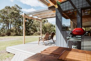 Eine Holzterrasse mit Grill und Stühlen, umgeben von Bäumen.