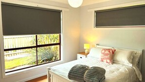 A bedroom with a large window, a bed with pillows, a bedside table with a lamp, and a hanging light fixture. - Seabreeze Retreat by the Beach (Sulphur Creek)