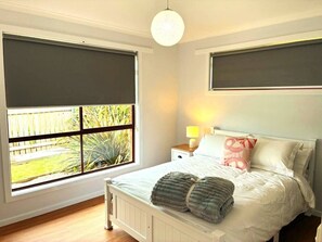 A bedroom with a large window, a bed with pillows, a bedside table with a lamp, and a hanging light fixture. - Seabreeze Retreat by the Beach (Sulphur Creek)