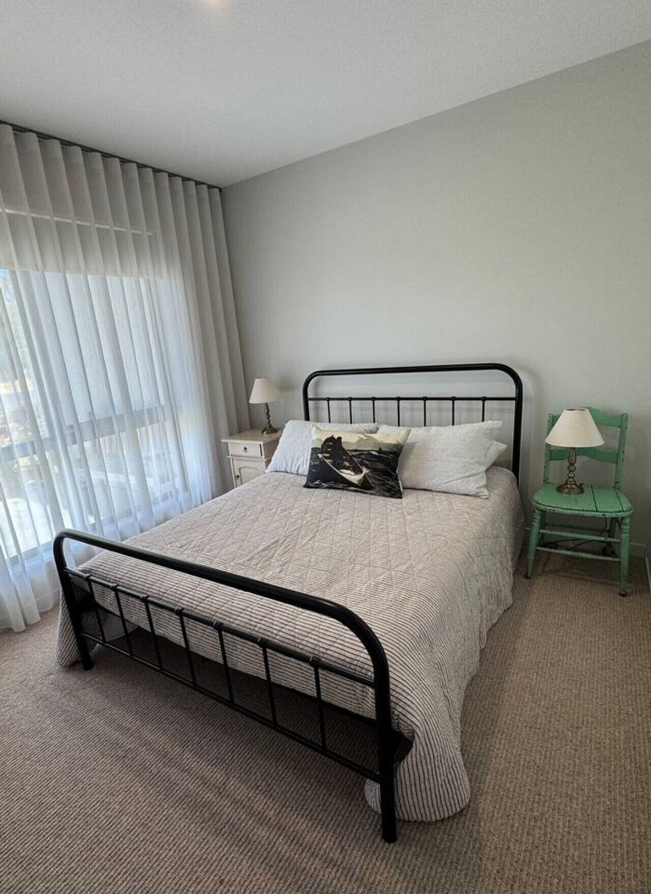 Une chambre à coucher avec un lit, une table de chevet, une chaise et une fenêtre avec des rideaux.