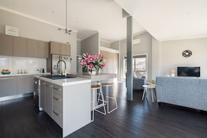 A modern kitchen with a central island, bar stools, a grey sofa, and a flat-screen TV. - The Family Beach Base, Port Sorell (Port Sorell)