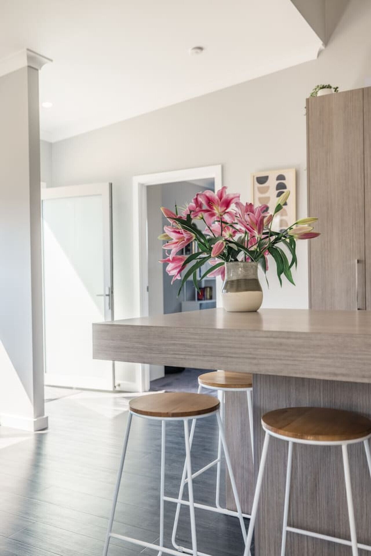 Cozinha moderna com bancada de madeira, dois bancos de bar brancos e um vaso com flores cor-de-rosa.