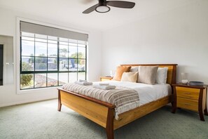 Ein Schlafzimmer mit einem hölzernen Bett, einem Nachttisch, einem Beistelltisch, einem Deckenventilator und einem großen Fenster mit Blick ins Freie.