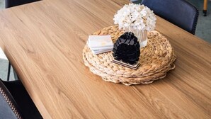 Ein Holztisch mit einer gewebten Tischmatte, einem schwarzen Dekorationsgegenstand und weißen Blumen.