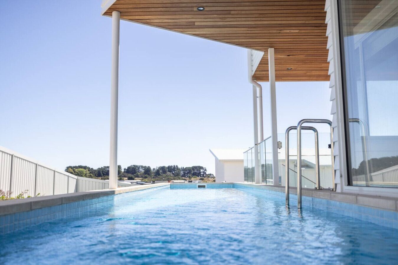 Une piscine surmontée d’une terrasse en bois, dotée de rampes en verre et offrant une vue dégagée sur le paysage environnant.