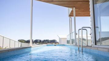 Une piscine surmontée d’une terrasse en bois, dotée de rampes en verre et offrant une vue dégagée sur le paysage environnant.